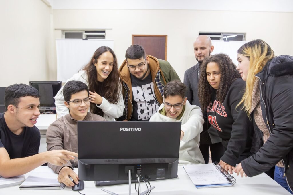 Grupo de alunos sorridentes reunidos em volta de um computador.